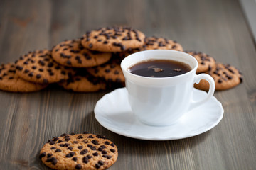 A stack of chocolate chip cookies around coffee cup on a wooden table