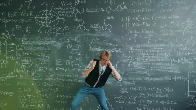 Funny young man student is dancing having fun near chalkboard with formulas enjoying successful education. People and positive emotions concept.