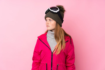 Ukrainian teenager skier girl with snowboarding glasses over isolated pink background looking side