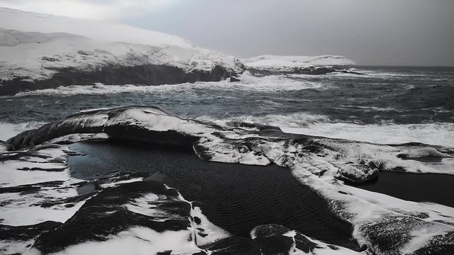The raging Barents Sea. Waves hit a snowy shore. Static natural background.