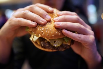 Close-up of man holding eating fastfood cheeseburger  
