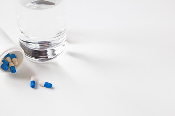 Pile of blue-white capsules and glass of water on white table. Course of treatment. Copy space.