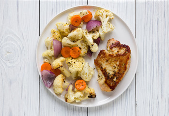 Turkey steak and vegetables cauliflower onion carrots baked in the oven on a white plate. Concept spring diet menu. Top view, flat lay