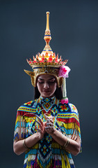Young lady wearing Thai Tradition southern costume ,made from colorful beads,put Headdress on her head,press hands together at her chest ,showing basic pattern folk dance,in front of solid backdrop.