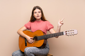 Fototapeta premium Ukrainian teenager girl with guitar over isolated background surprised and pointing finger to the side