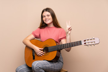 Ukrainian teenager girl with guitar over isolated background smiling and showing victory sign