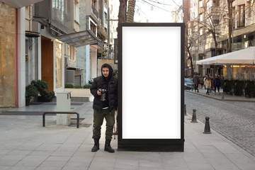 Fototapeta premium Young photographer stands in front of an empty billboard while taking pictures on the street