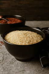 Bowls with rice, spoon and towel on grey table, close up