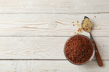 Fototapeta na wymiar Bowl with rice and spoon on wooden background, top view