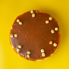 Hazelnut and cream cheese cake with salted caramel as a decoration on bright yellow background, directly above view