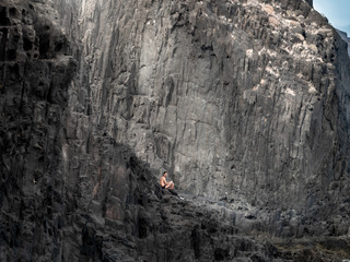 Conceptual image of lonely naked man sitting on the cliffs at ocean coast