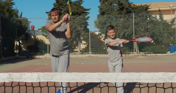 Child traning in tennis. Father and son practice blows in tennis on coart. Active leisure together.