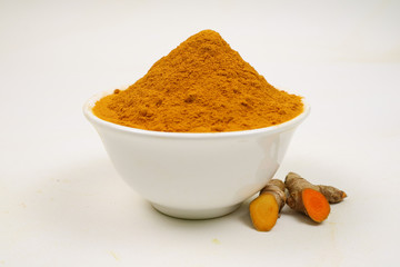 Turmeric powder in a white cup and turmeric roots isolated on a white background, used as a tonic...