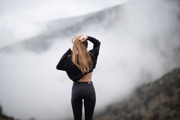 blone girl standing and looking at a fog on a mountain
