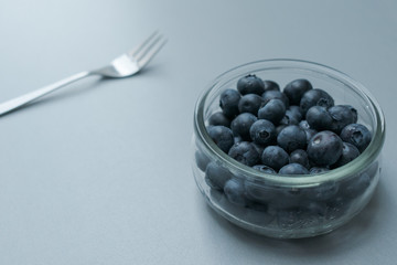 Delicious transparent glass bowl of fresh organic blueberries and a fork on a modern kitchen countertop
