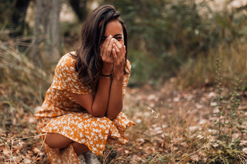 Young smiling woman squatting in the forest wearing a dress