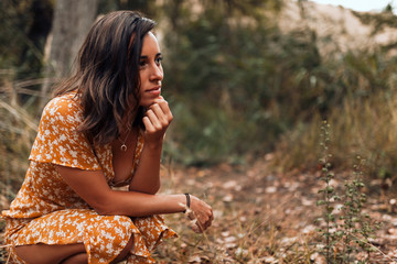 Young smiling woman squatting in the forest wearing a dress