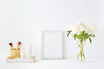 Home interior with decor elements. White frame, white peonies in a vase, cosmetic set
