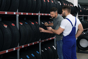 Obraz na płótnie Canvas Mechanic helping client to choose car tire in auto store