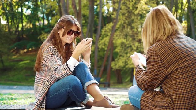 Happy girls browsing photos in social media sitting in green park