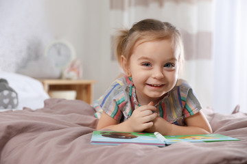 Naklejka premium Cute little girl with book on bed at home