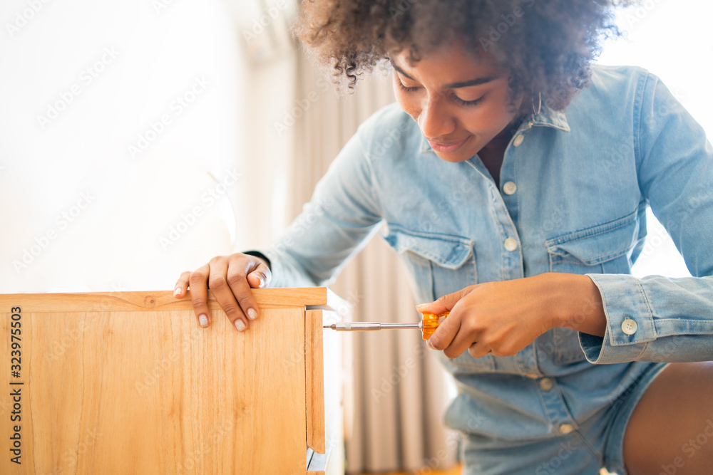 Wall mural Afro woman repairing furniture at home.