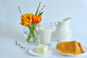 thin pancakes and glass of milk on the table near a vase with tulips on a white background.Pancake week: pancakes with butter and tea on white table.french crepes .