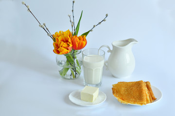 thin pancakes and glass of milk on the table near a vase with tulips on a white background.Pancake week: pancakes with butter and tea on white table.french crepes .