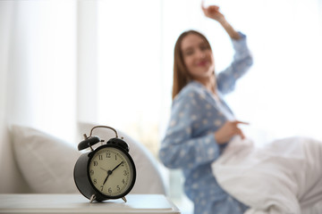 Young woman stretching at home in morning, focus on alarm clock