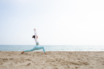 Fit girl doing yoga in the beach by the sea on a sunny day