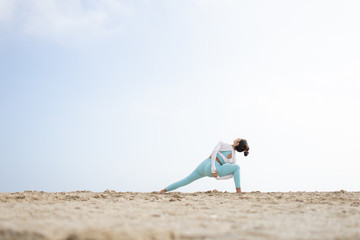 Fit girl doing yoga in the beach by the sea on a sunny day