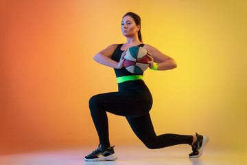 Fototapeta na wymiar Young caucasian plus size female model's training on gradient orange background in neon light. Doing workout exercises with ball. Concept of sport, healthy lifestyle, body positive, equality.