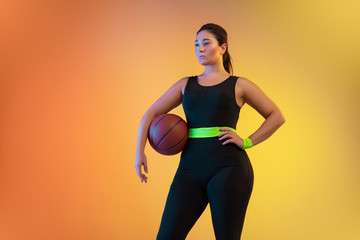 Fototapeta na wymiar Young caucasian plus size female model's training on gradient orange background in neon light. Posing confident with the ball. Concept of sport, healthy lifestyle, body positive, equality. Copyspace.