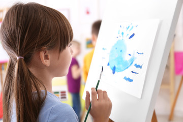 Cute little child painting during lesson in room