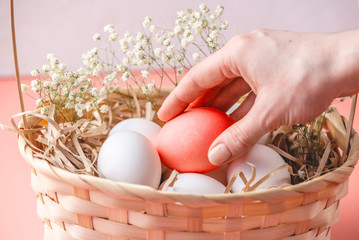 Bright red Easter egg among white ones in a basket on a light background. Festive spring card