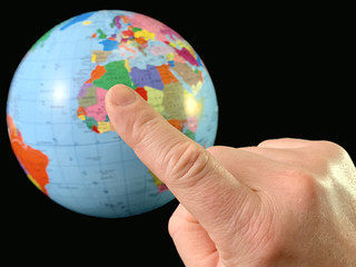 Index finger points to a globe, on a black background. Touching a finger to the globe. A man holds his hand in the direction of the world map. Concept: travel, tourism