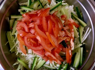 Green salad of cabbage, cucumbers and tomatoes, on a black background. Cutting vegetables in a metal bowl. Finely chopped vegetables for salad. Concept: vegetable diet, healthy nutrition.