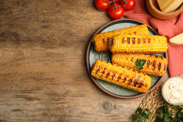 Delicious grilled corn cobs on wooden table, flat lay. Space for text