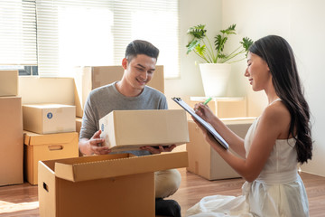 Young Asian married couple helping packing and checking together and woman checking stuff by using...