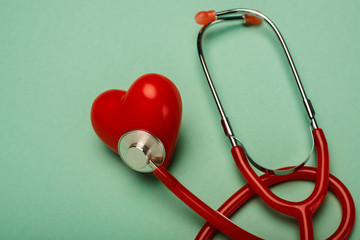 Red stethoscope connected with decorative heart on green background, world health day concept