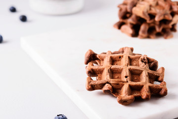 Homemade Chocolate waffles, milk and blueberries on white marble tray. Breakfast. Selective focus