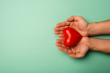 Top view of man holding decorative red heart on green background, world health day concept