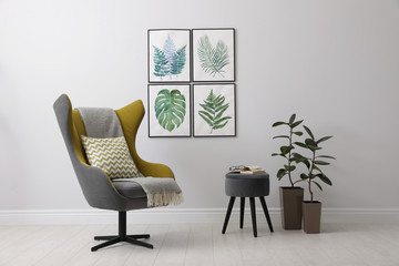 Stylish room interior with comfortable armchair and paintings of tropical leaves