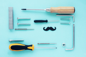 .flat layout top view: screwdrivers of different sizes, bolts, staples for a construction gun, black shiny mustache. space for text.