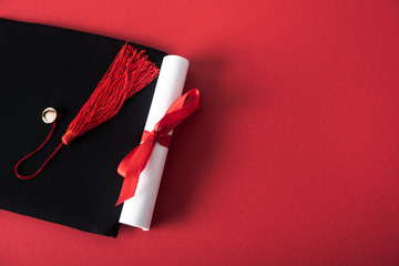 Fototapeta Top view of diploma with beautiful bow and graduation cap with tassel on red background obraz