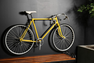 Fototapeta na wymiar Yellow bicycle hanging on black wall indoors