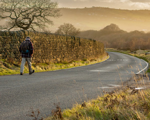 A senior strides out for a sunny early morning walk along the road across Baildon Moor