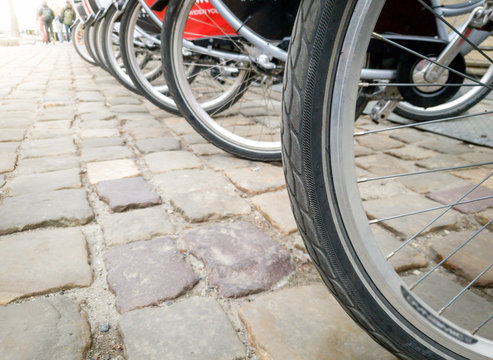 Closeup image of long row of bicycle wheels on cobblestone square at old city
