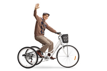 Happy elderly man riding a tricycle and waving at camera - obrazy, fototapety, plakaty