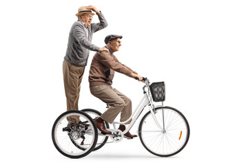Elderly man riding a tricycle and a senior gentleman standing behind